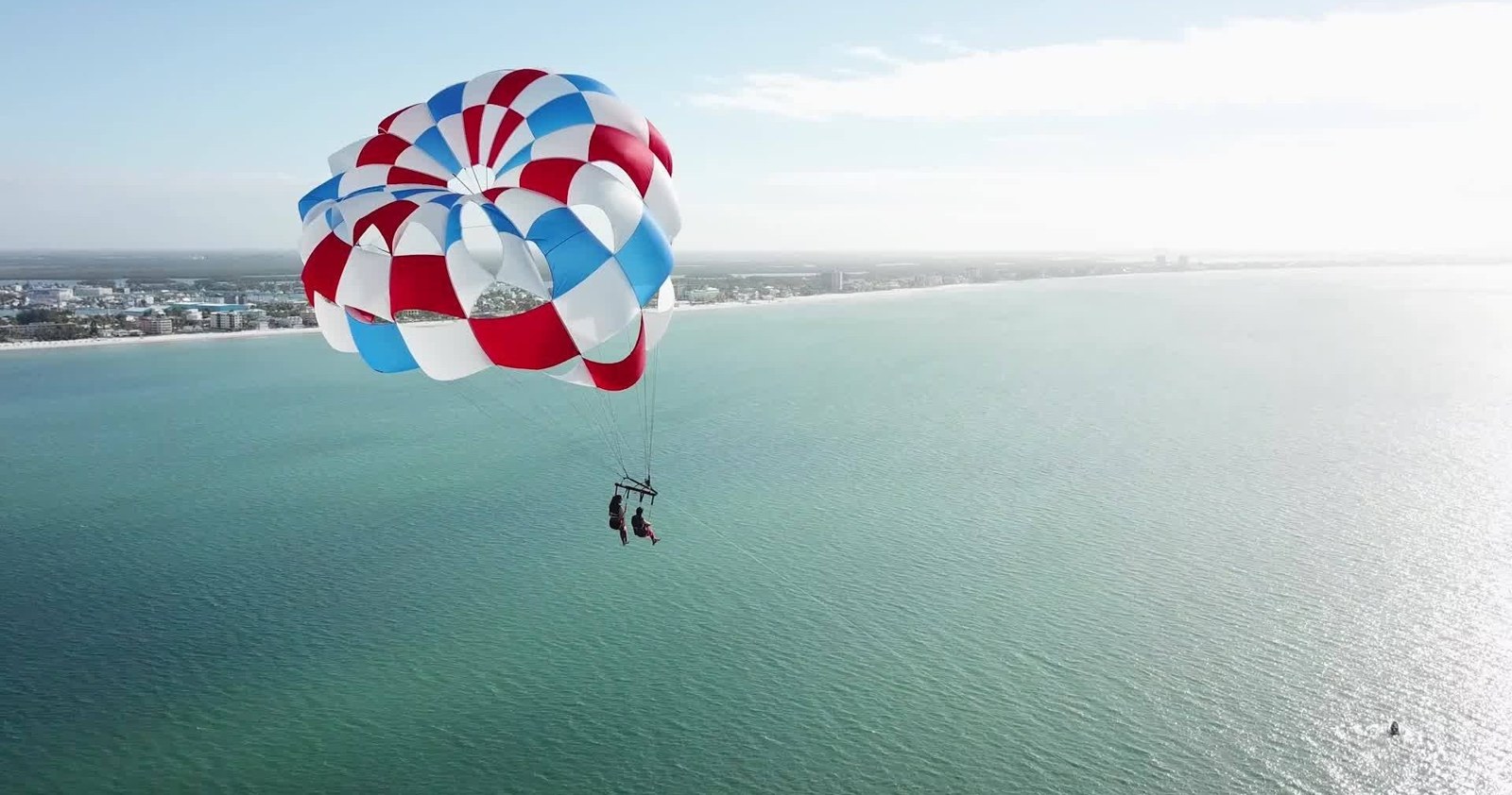 Two people parasailing beneath a red, white and blue canopy above coastal water on Fort Myers Beach