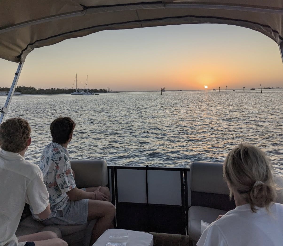 Guests seated aboard a covered boat watching the sun set over the water