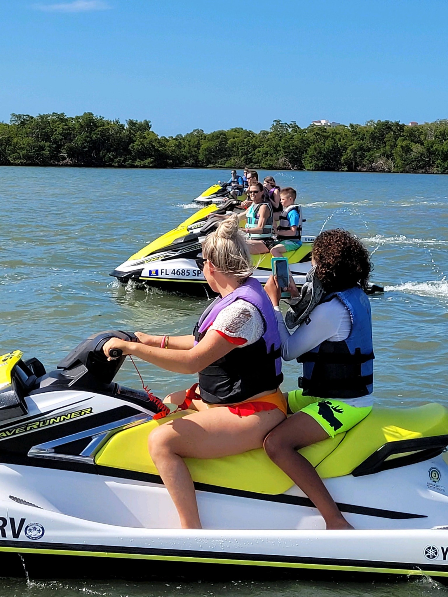 Guests wearing life jackets on yellow WaveRunners together beside a mangrove shoreline